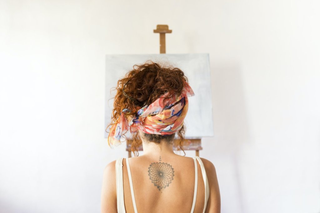 Rear view of young female painter in art studio in front of empty canvas